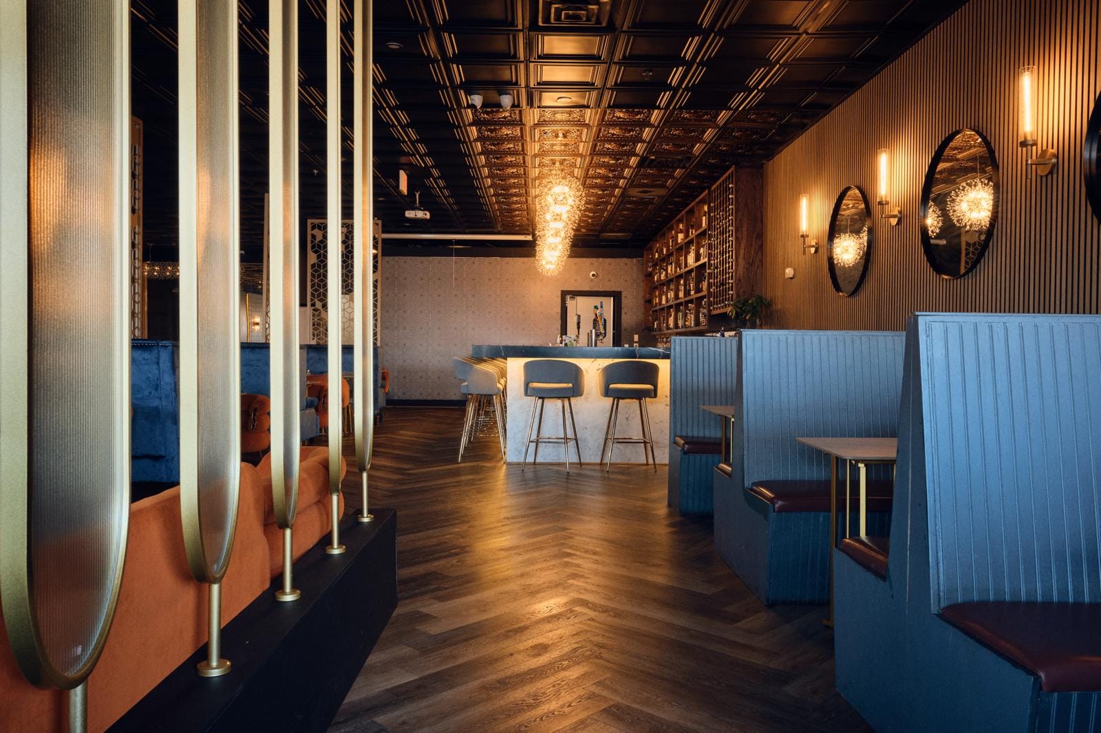 Full dining room - gold columns, herringbone floor, glowing bar in depth